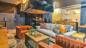 A modern living room with a sofa, armchairs, and a coffee table. There is a television and a sound system on the wall. - Pool- Hot Tub- Bar! Rooftop Fire Pit 9 Beds (Nashville)