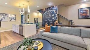A modern living room with a sofa, a coffee table, and a kitchen area in the background. - Pool- Hot Tub- Bar! Rooftop Fire Pit 9 Beds (Nashville)