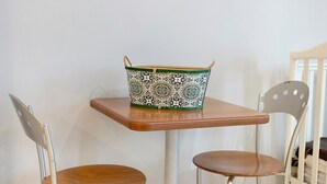Une petite table sur laquelle repose un panier décoré, deux chaises et, au fond, un berceau.