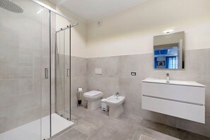 Een moderne badkamer met een douchecabine van glas, toilet, bidet en een wastafelmeubel met spiegel.