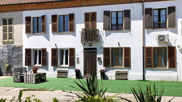 Un edifici blanc amb nombroses finestres i persianes, un jardí amb gespa i mobles d'exterior.