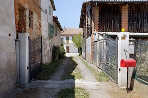 Un estrecho callejón con un buzón rojo, una verja de metal y un edificio de ladrillo con techo de tejas.