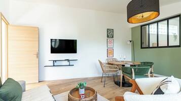 A modern living room with a flat-screen TV, wicker furniture, a round wooden coffee table, and a large window.