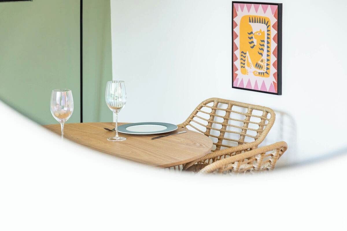 Een eettafel met twee wijnglazen, een bord en een vork. Een rieten stoel staat bij de tafel.