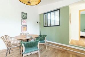 A dining area with a round table, two wicker chairs, and a green wall with a window.