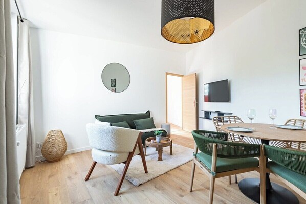 A modern living room with a sofa, a dining table with chairs, a TV, and a large mirror on the wall.