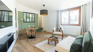 Ein modernes Wohnzimmer mit einer Couch, einem Esstisch mit Stühlen, einem Fernseher und einem großen Fenster.