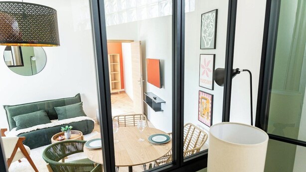 Ein modernes Zimmer mit einer Couch, einem Esstisch, Stühlen, einer Lampe und Kunstwerken an der Wand.