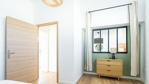Ein Schlafzimmer mit Holztür, Nachttisch mit Lampe, Spiegel und einem gewebten Teppich.