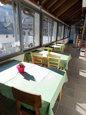 A restaurant with tables and chairs, large windows, and a view of buildings outside. - Guest House '1 Polse Di San Pieri Camera Han' with Shared Terrace, Shared Garden and Wi-Fi (Zuglio)