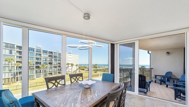 A modern dining area with a wooden table, blue chairs, and a view of the ocean and buildings. - Captains Quarters 318: charming, steps to ocean and pool (Saint Augustine)