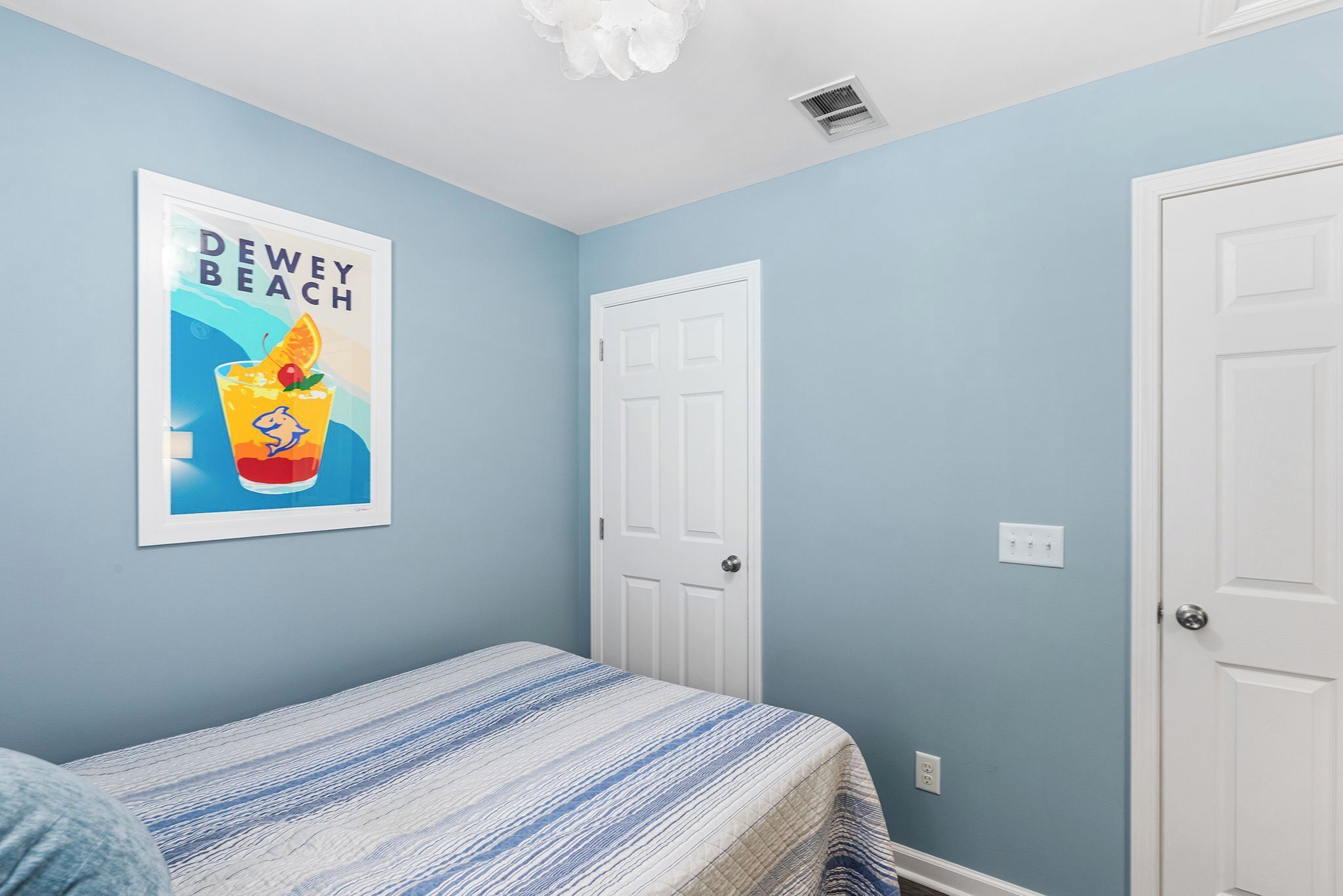 A bedroom with a bed, a framed poster, and two white doors.