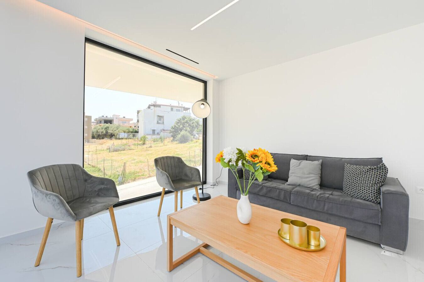 A modern living room with a grey sofa, two armchairs, a wooden coffee table, and a vase with sunflowers.
