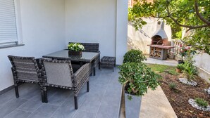 A patio with a table and chairs, a small garden, and a barbecue area. - Apartment Perla (Vir)