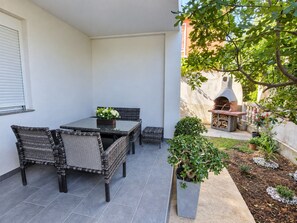 A patio with a table and chairs, a small garden, and a barbecue area. - Apartment Perla (Vir)