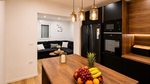 A modern kitchen with a wooden island, black appliances, and a black sofa in the background. - Apartment Perla (Vir)
