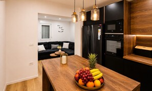 A modern kitchen with a wooden island, black appliances, and a black sofa in the background. - Apartment Perla (Vir)