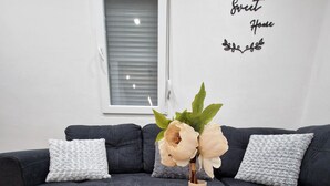 Un soggiorno moderno con un divano blu scuro, due tavolini rotondi in legno e un vaso con fiori.