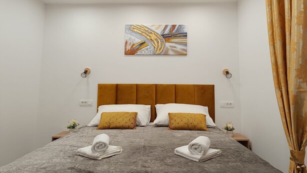 Camera d'albergo con un letto grande, due cuscini, una testiera, un'opera d'arte a parete, lampade da comodino e una tenda.