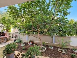 A patio area with a tree, a barbecue grill, and various potted plants. - Apartment Perla (Vir)