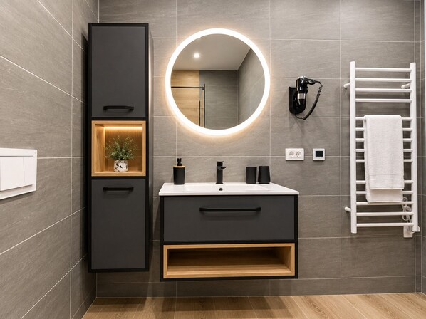 Une salle de bain moderne avec un meuble-lavabo, un miroir doté d’un éclairage circulaire, un porte-serviettes et une plante posée sur le meuble-lavabo.