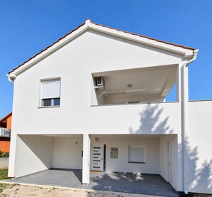 A two-story building with a flat roof, a small balcony on the upper floor, and a garage entrance. - Apartment Perla (Vir)
