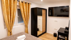 A hotel room with a bed, a TV, a wooden wardrobe, and a window with curtains. - Apartment Perla (Vir)