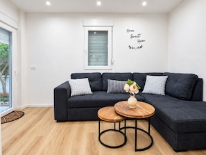 A modern living room with a dark grey sectional sofa, a small wooden coffee table, and a decorative vase with flowers. - Apartment Perla (Vir)