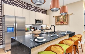 A modern kitchen with a central island, stainless steel appliances, and a dining area with wicker chairs. - Pool - Hot Tub - Golf-Fire pit 14 Beds (Nashville)