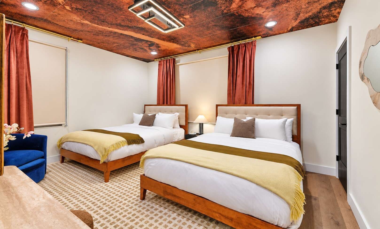 Une chambre d’hôtel avec deux lits, un fauteuil bleu et un tapis à motifs.