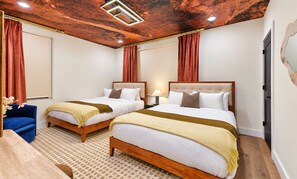 Een hotelkamer met twee bedden, een blauwe fauteuil en een kamerbreed tapijt met een patroon.
