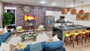 A modern living room with a sofa, coffee table, and chairs, a kitchen with a refrigerator and microwave, and a dining area with bar stools. - Ultra Lux Home - Pool - Hot Tub - Fire pit! 14 Beds (Nashville)