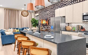 Een moderne keuken met een centraal eiland, roestvrijstalen apparatuur en een blauwe bank in de woonkamer.