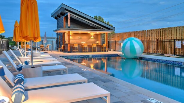 A pool area with lounge chairs, a bar, and a wooden fence. - Ultra Lux Home - Pool - Hot Tub - Fire pit! 14 Beds (Nashville)