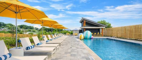 Un área junto a la piscina con sillones de descanso, sombrillas y una pileta.