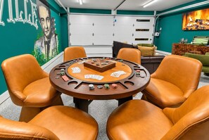 Une pièce comprenant une table de poker, des fauteuils en cuir, un mur vert orné d’une fresque et une cheminée.