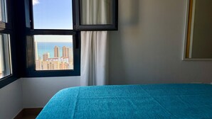 Une chambre avec un lit, une fenêtre avec des rideaux et une vue sur les bâtiments et la mer.