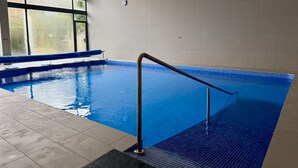 Une piscine intérieure à l'eau d'un bleu limpide, dotée d'un sol carrelé et d'une rambarde de sécurité en métal.