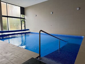 Ein Innenpool mit klarem, blauem Wasser, gefliestem Boden und einem Metallgeländer.