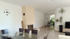 Een moderne eetruimte met een glazen tafel en donkere stoelen, een witte bank en een televisie in een hoek.