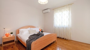 A neatly arranged bedroom with a wooden bed, a bedside table with a lamp, and a window with sheer curtains.