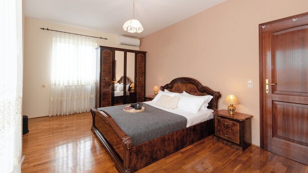 A bedroom with a wooden bed, a nightstand with a lamp, a wardrobe, and a mirror.