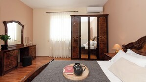 A hotel room with a wooden desk, a bed with white linens, a bedside table with a lamp, and a wardrobe with a mirror.