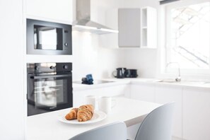 Una cocina moderna con armarios blancos, un horno negro y un comedor con una mesa y sillas blancas.