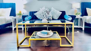 Un soggiorno moderno con un tavolino in vetro, divani blu e un quadro appeso al muro.