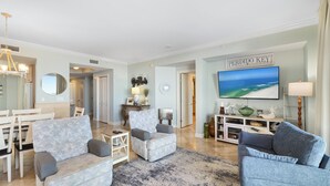 A spacious living room with a large painting, a dining area with a white table and chairs, and a cozy seating area with a patterned sofa and armchairs. - Indigo West 304 by Liquid Life (Pensacola)