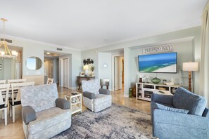 A spacious living room with a large painting, a dining area with a white table and chairs, and a cozy seating area with a patterned sofa and armchairs. - Indigo West 304 by Liquid Life (Pensacola)