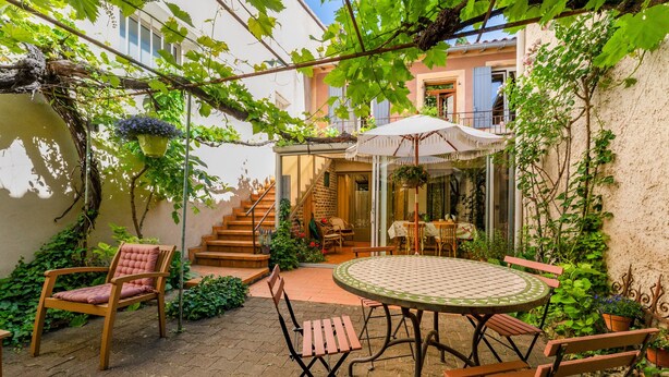 A patio with a round table and chairs, a wooden chair, a hanging plant, and a staircase leading to an upper level. - Room 'Parfum De Soleil' with Shared Terrace, Shared Garden and Wi-Fi (Bédoin)