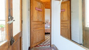 A hallway with wooden doors, a tiled floor, and a bed with a floral bedspread in the background. - Room 'Parfum De Soleil' with Shared Terrace, Shared Garden and Wi-Fi (Bédoin)