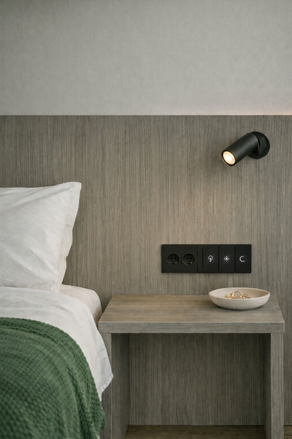 Un dormitorio moderno con cama, mesita de noche y lámpara fijada a la pared.